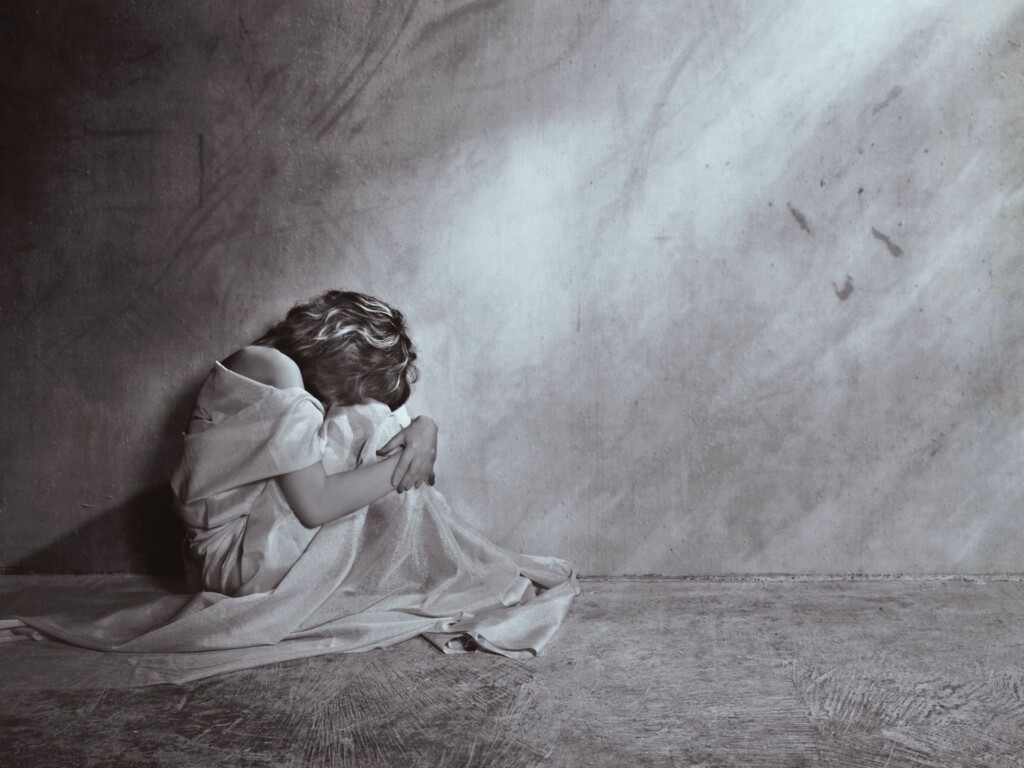 An image of a woman sitting alone on the floor and hiding her face because of shame